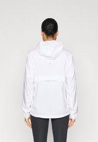 Jachetă albă cu glugă, croială lejeră, mâneci lungi și design cu panou posterior. Textură netedă și șnur ajustabil la glugă.