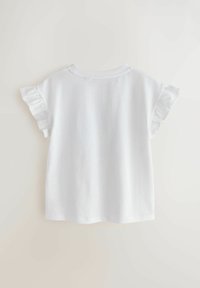 Camisa blanca de manga corta con mangas con volantes, mostrada contra un fondo uniforme de color blanco hueso, vista desde atrás.