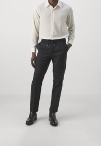 Ljust beige skjorta med knappar och textilstruktur, i kombination med svarta cargobyxor med dragsko i midjan och sidofickor. Svarta ankelboots.