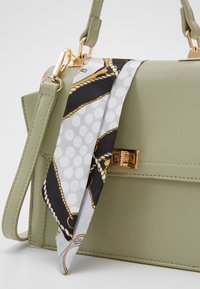 Bolso de mano de imitación cuero verde con un cierre en tono dorado, bufanda estampada extraíble con acentos en gris, negro y dorado, y una correa ajustable.
