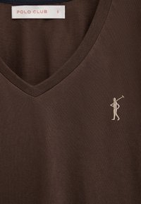 Bruin V-hals shirt met een kleine geborduurde afbeelding van een persoon die een polo mallet vasthoudt op de borst en een witte "POLO CLUB" label.