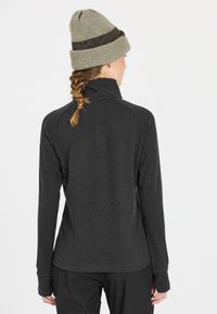 Dunkelgraues Langarmshirt mit hohem Kragen und Raglanärmel, kombiniert mit einer hellgrünen Strickmütze mit einem dunkelbraunen Streifen.
