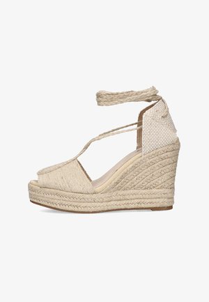 Sandalia de cuña beige de esparto con parte superior de yute trenzado, puntera abierta, correas al tobillo y tacón texturizado. Presenta un acento de tela tejida en la parte trasera.
