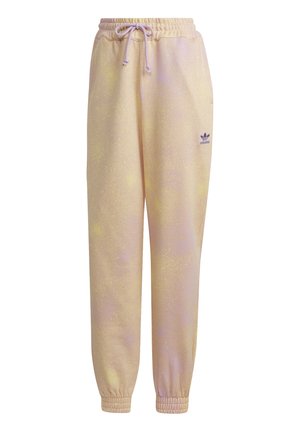Jasnobeżowe spodnie dresowe Adidas z elastycznymi mankietami, ściągaczem w pasie, bocznymi kieszeniami oraz fioletowym logo Adidas na lewym udzie.