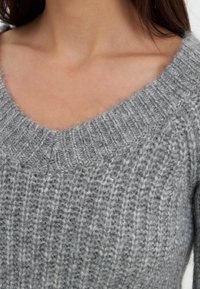 Szary dzianinowy sweter z dekoltem w serek. Miękka tekstura, z prążkowanym wzorem i luźnym krojem, który delikatnie opada wokół dekoltu.