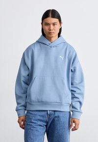 Lyseblå hoodie lavet af blødt stof, med en kængurulomme og et hvidt logo på venstre bryst. Løs pasform med ribbede manchetter.