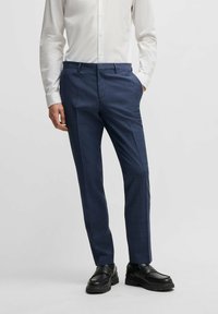 Marineblaue, maßgeschneiderte Hose aus strukturiertem Stoff, mit schmalem Schnitt, vorn gefaltet und seitlichen Taschen, kombiniert mit schwarzen Schuhen.