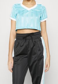 Person som bär en ljusblå, kort Adidas sporttröja och svarta träningsbyxor med ljusblå och vita sidostripes.