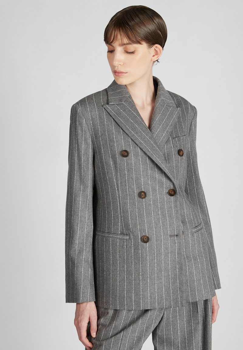 Blazer grigio doppiopetto con sottili righe bianche. Presenta rever a punta, due tasche frontali e bottoni marroni. Vestibilità tailored.