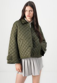 Giacca cropped imbottita di colore verde oliva, con colletto, chiusura a bottoni e maniche oversize. Presenta tasche laterali e una superficie liscia.