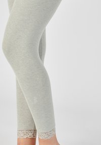 Lichtgrijze leggings met een gladde textuur, voorzien van een kantafwerking bij de enkel voor extra detail. Strakke pasvorm met een slanke silhouette.
