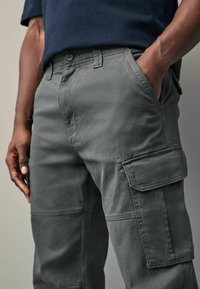 Graue Cargo-Hosen mit lockerer Passform, mehreren Taschen und Knopfverschluss, gefertigt aus weichem Baumwollstoff mit glatter Textur.