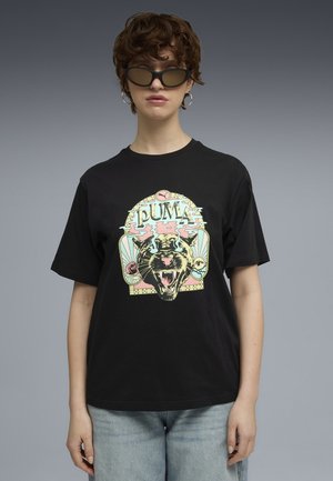 Sort bomulds t-shirt med et farverigt grafik af en brølende panter med stiliseret tekst. Kombineret med lyseblå denimbukser.