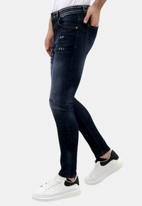 Donkerblauwe skinny jeans met versleten details, voorzien van een klassiek vijf-pocket ontwerp en een versleten textuur, gecombineerd met witte sneakers.