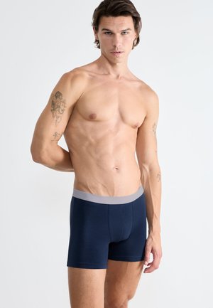 Boxer blu navy realizzati in un morbido tessuto con un elastico grigio chiaro in vita. Presentano una vestibilità aderente e un design classico.