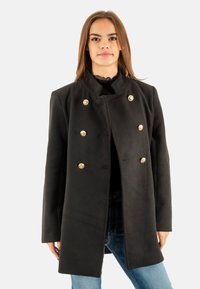 Abrigo de lana negro con un cuello alto y un frente de doble botonadura, que presenta botones en tono dorado y una silueta recta. Mangas largas.