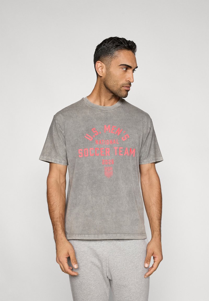 Šedé bavlněné tričko s červeným nápisem "U.S. MEN'S NATIONAL SOCCER TEAM 2026", kulatým výstřihem a krátkými rukávy.