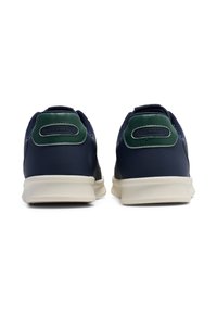 Marinblå sneakers med gröna accenter. Slät syntetisk ovandel, texturerade bakpaneler och ljus gummisula. "Hummel"-logotyp på hältabby.