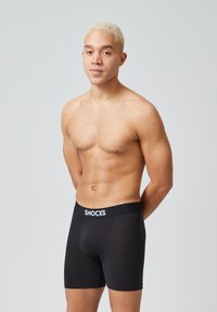 Boxer briefs neri con una cintura elastica logo. Design semplice, texture liscia e forma aderente. Il modello è senza maglietta, mostrando il prodotto.