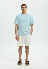 Ljusblå bomulls t-shirt med rund halsringning, korta ärmar, kombinerad med krämfärgade linshorts och svarta slide-sandaler.