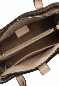 Intérieur de sac à main noir et beige avec un grand compartiment central, une poche zippée et deux poches supplémentaires. Texture lisse, doublure en tissu.