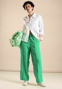 White button-up shirt, green linen wide-leg pants, and a patterned green and white bag. Sneakers complete the outfit.