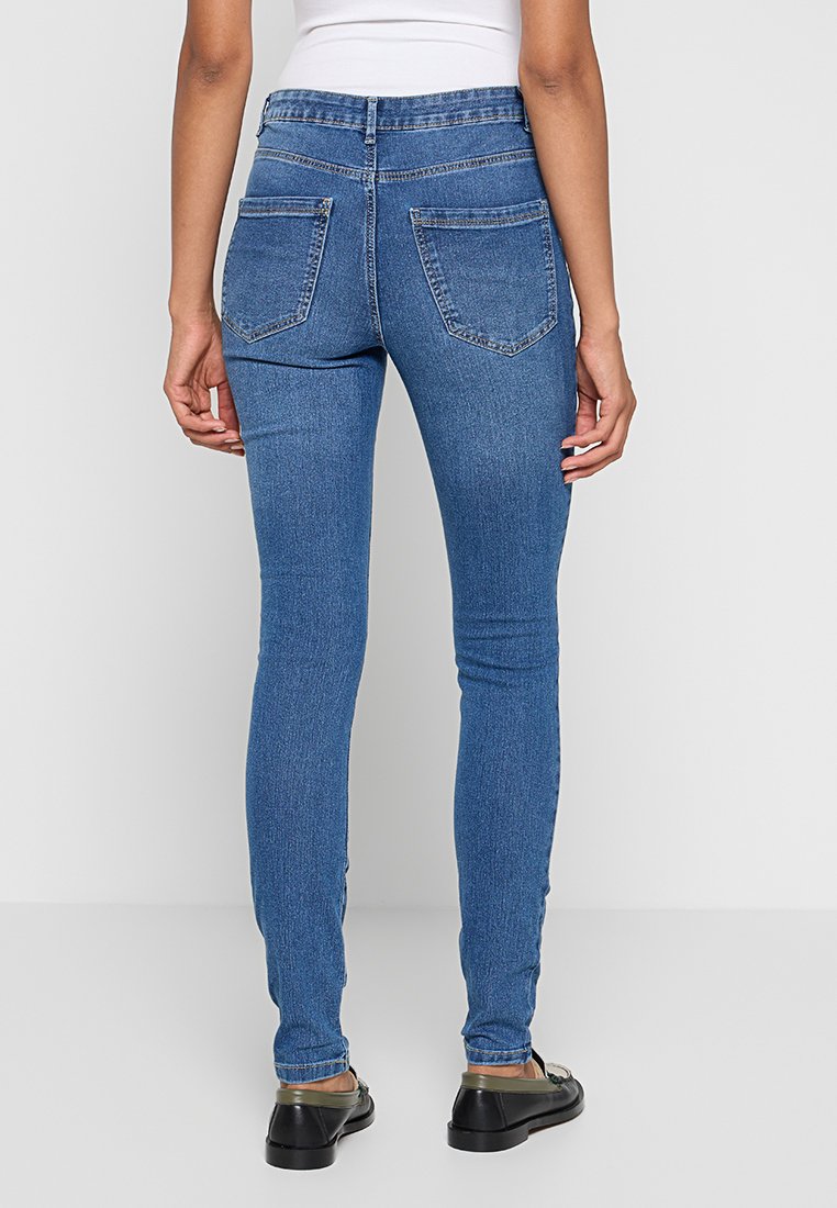 Dünne blaue Jeans mit hoher Taille, zwei Gesäßtaschen und engem Beinabschluss. Der Stoff wirkt glatt mit minimaler Abnutzung.