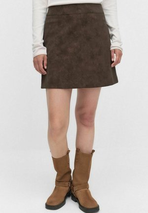 Jupe mini en daim brun avec une texture lisse, présentant une taille ajustée et une forme évasée. Associée à des bottes marron jusqu'aux genoux avec des boucles.