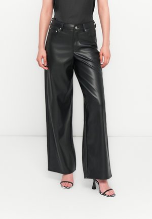 Zwarte neplederen wijde broek met hoge taille, voorzien van steekzakken en zilverkleurige accenten, gecombineerd met zwart-witte haksandalen.