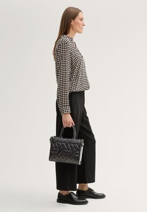 Top à motif pied-de-poule noir et blanc, coupe décontractée, associé à un pantalon large noir. Tient un sac en cuir matelassé noir avec deux anses.
