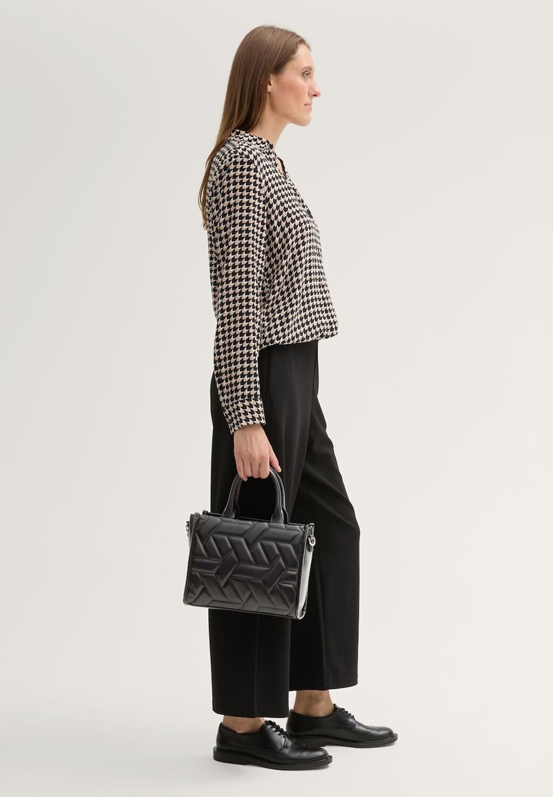 Zwart-wit houndstooth patroon top, met een ontspannen pasvorm, gecombineerd met zwarte wijde broek. Houdt een zwarte gewatteerde handtas met dubbele handvatten vast.