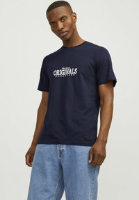 Camiseta de algodón azul marino de manga corta, con el texto blanco "Originals Worldwide" impreso en la parte frontal. Textura suave y corte regular.