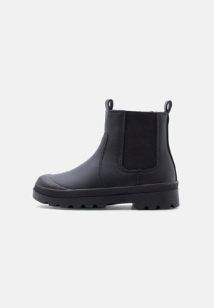 Bottine Chelsea noire montant à la cheville avec des panneaux élastiques sur les côtés, des languettes à l'avant et à l'arrière, et une semelle épaisse à crampons.