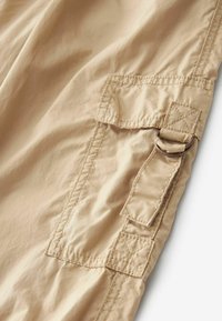 Beiga cargobyxor tillverkade av ett lätt material, med en stor ficka med klaff och ett metallringdetalj på sidan.