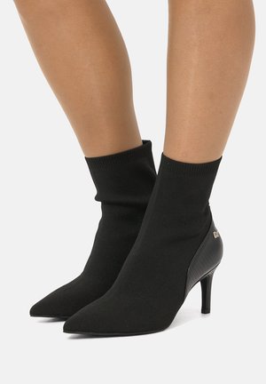 Stivaletti neri alla caviglia con parte superiore in maglia, punta affusolata e tacco a stiletto. Presentano pannelli laterali testurizzati e un dettaglio logo minimalista.