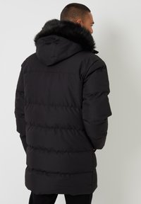Czarna kurtka puchowa z kapturem wykończonym futrem, z pikowanym wzorem, długimi rękawami i lekko wygiętym dołem z tyłu.