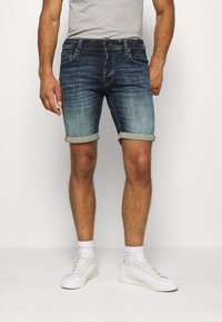 Shorts de denim en azul oscuro con un acabado desgastado y dobladillos rematados. Presenta un estilo clásico de cinco bolsillos y una cremallera con un cierre de botón.