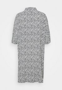 Robe blanche à manches courtes avec motif de points noirs irréguliers, vue de dos sur un fond uni.