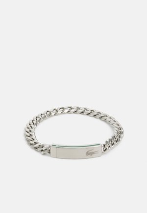 Pulseira de corrente em prata com um fecho de metal plano e gravado, destacando um detalhe verde. Os elos são arredondados e polidos para um acabamento suave.