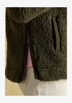 Olijfgroene fleecejas met een gestructureerd oppervlak, zijzakken en een korte rits. De binnenkant heeft een contrasterende roze laag.