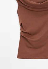 Top marrone a maniche corte realizzato in tessuto morbido, caratterizzato da dettagli drappeggiati nella parte superiore e una texture liscia.