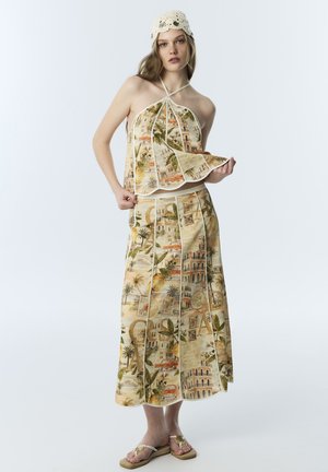 Junge Frau, die ein Neckholder-Top und einen passenden langen Rock mit Vintage-Architektur- und botanischem Muster trägt, kombiniert mit Sandalen und einer gehäkelten Mütze.