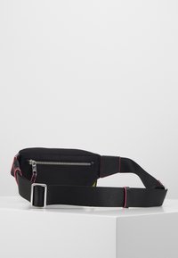 Musta nailonivyötasku, jossa on vaaleanpunaista ompeletta, hopeiset vetoketj yksityiskohdat, säädettävä hihna ja ohut muotoilu. Monikäyttöinen ja käytännöllinen muotoilu.