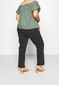 Top verde de hombros descubiertos con mangas abullonadas, combinado con pantalones negros y sandalias de tacón marrones. Tela suave y ajuste relajado visibles.