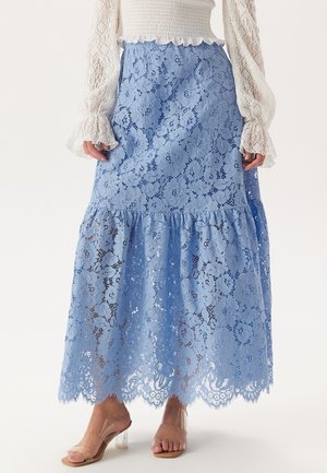 Blå spets maxikjol med blommönster, en lager-på-lager volangkant och en halvgenomskinlig textur. Matchad med klara klackar.