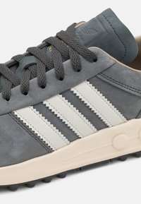 Sneaker in suede grigio con strisce in pelle bianca, lacci grigi testurizzati, suola beige chiaro e collarino imbottito con dettagli del logo.