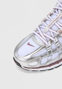 Α θλητικό παπούτσι σε ασημί και λευκό χρώμα με υλικό από δίχτυ, περίτεχνο σύστημα κορδονιών και το χαρακτηριστικό λογότυπο Nike στο πλάι. Λαστιχένια σόλα.