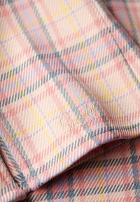 Gros plan d’un tissu à carreaux rose, bleu et jaune avec un texte brodé subtil lisant "Stay Wild."