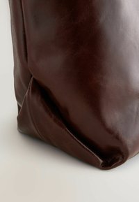 Braune Lederhandtasche mit glatter Textur, weichen Falten und rundem Design. Verfügt über einen subtilen Glanz und ein minimalistisches Design.
