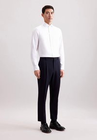 Witte shirt met lange mouwen en een opstaande kraag, gecombineerd met donkerblauwe, op maat gemaakte broek en zwarte leren schoenen. Soepele texturen, nauwsluitend ontwerp.